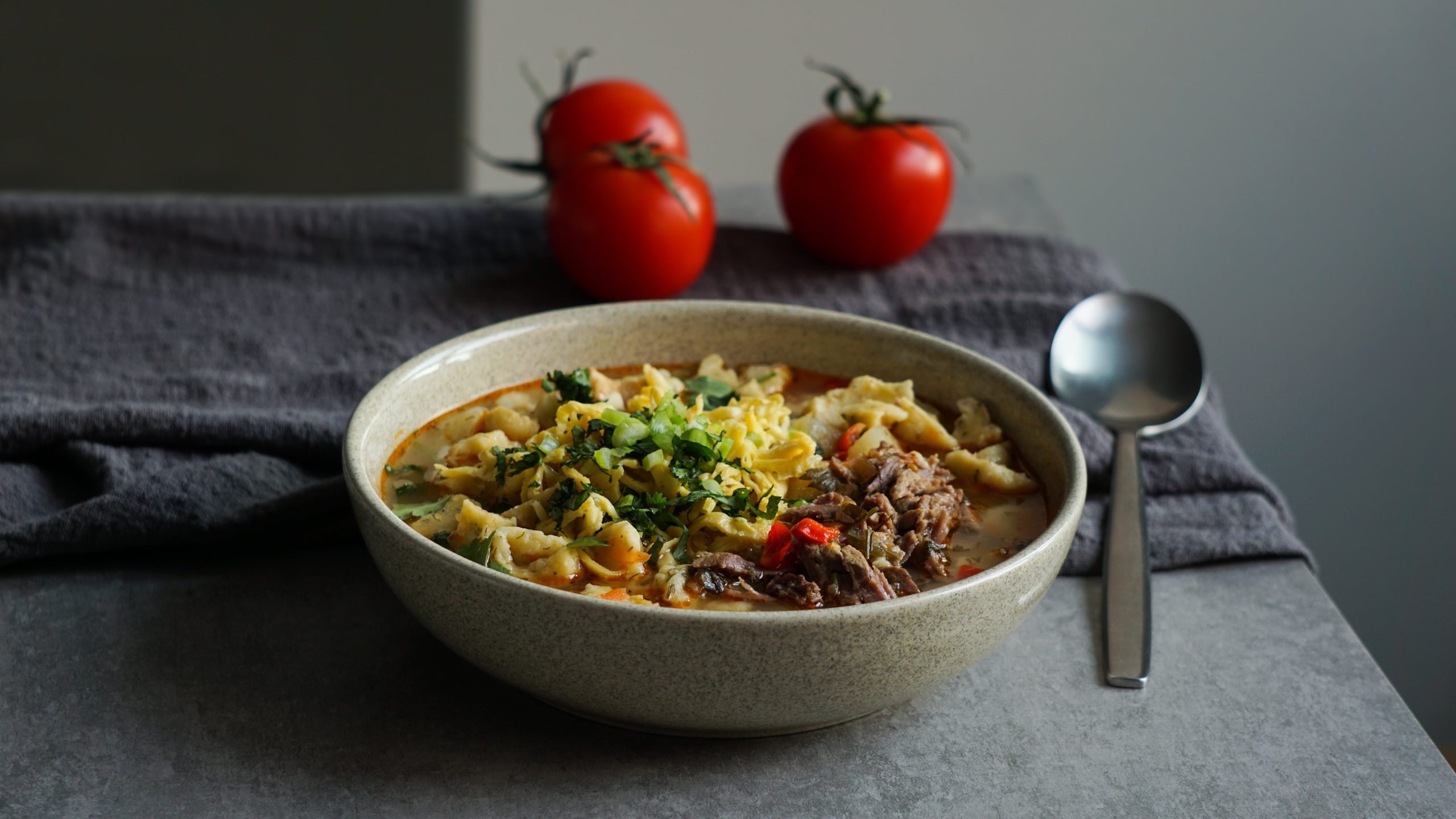 prato com sopa de macarrão e carne. Ao lado, dois tomates e uma colher